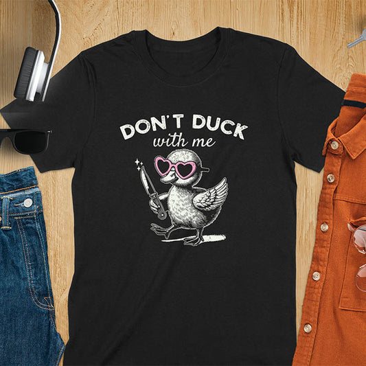 A T-shirt with a cartoon duck wearing heart-shaped sunglasses and holding a knife. The text above reads DON'T DUCK with me. The design is humorous and edgy, combining playful imagery with a bold statement.