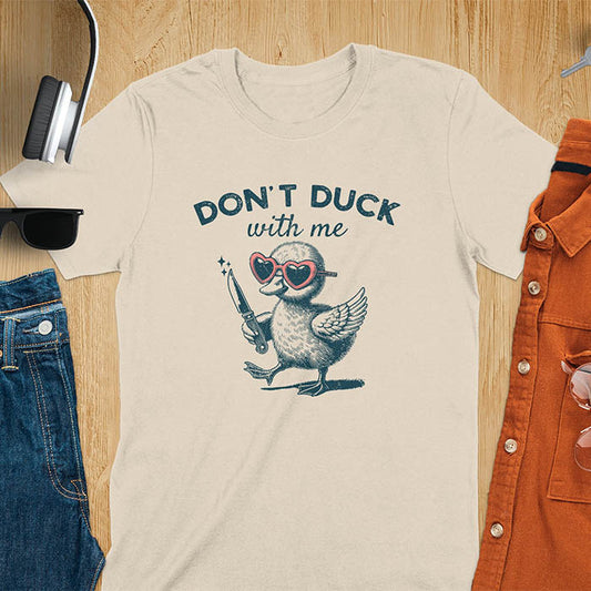 A T-shirt with a cartoon duck wearing heart-shaped sunglasses and holding a knife. The text above reads DON'T DUCK with me. The design is humorous and edgy, combining playful imagery with a bold statement.