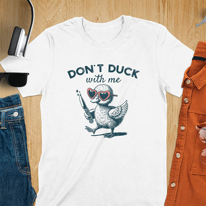 A T-shirt with a cartoon duck wearing heart-shaped sunglasses and holding a knife. The text above reads DON'T DUCK with me. The design is humorous and edgy, combining playful imagery with a bold statement.