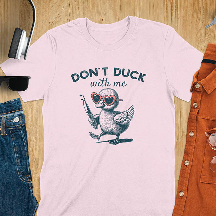 A T-shirt with a cartoon duck wearing heart-shaped sunglasses and holding a knife. The text above reads DON'T DUCK with me. The design is humorous and edgy, combining playful imagery with a bold statement.