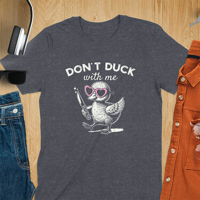 A T-shirt with a cartoon duck wearing heart-shaped sunglasses and holding a knife. The text above reads DON'T DUCK with me. The design is humorous and edgy, combining playful imagery with a bold statement.