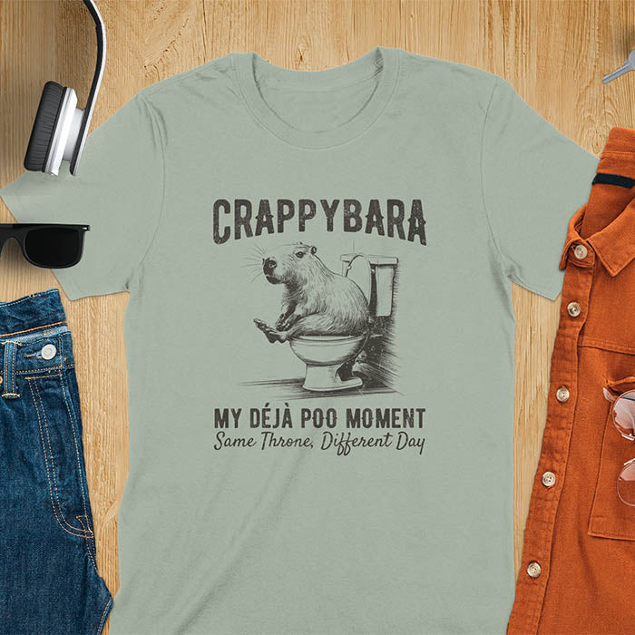 A humorous graphic of a capybara sitting on a toilet with the text Crappybara above and Déjà Poo Moment: same throne, different day below. A funny design for animal and meme lovers.