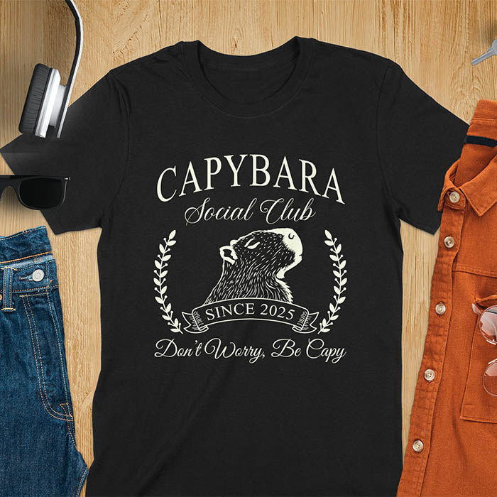 A capybara illustration within a laurel wreath and banner that reads Capybara Social Club Since 2025 and Don't Worry, Be Capy. A retro-inspired design.