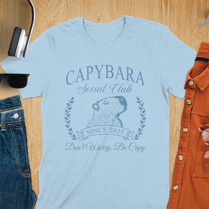 A capybara illustration within a laurel wreath and banner that reads Capybara Social Club Since 2025 and Don't Worry, Be Capy. A retro-inspired design.