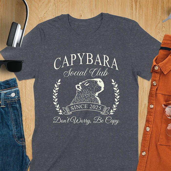 A capybara illustration within a laurel wreath and banner that reads Capybara Social Club Since 2025 and Don't Worry, Be Capy. A retro-inspired design.