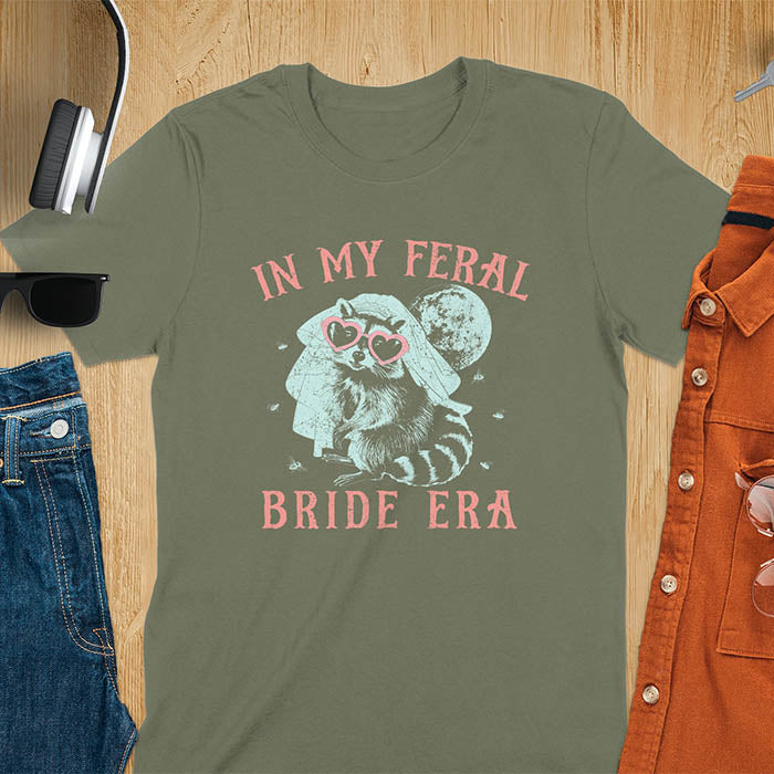 A raccoon wearing heart-shaped sunglasses and a bride's veil, with the moon in the background. Text reads In My Feral Bride Era.