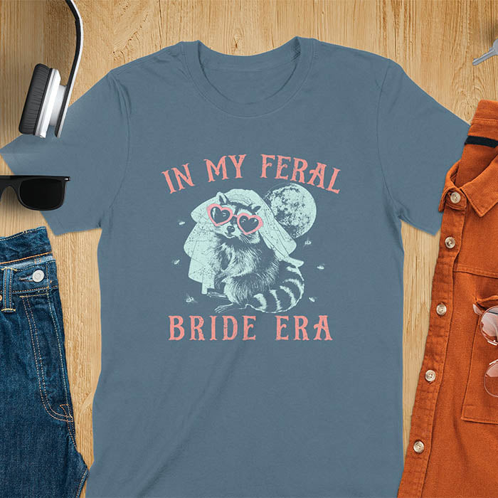 A raccoon wearing heart-shaped sunglasses and a bride's veil, with the moon in the background. Text reads In My Feral Bride Era.