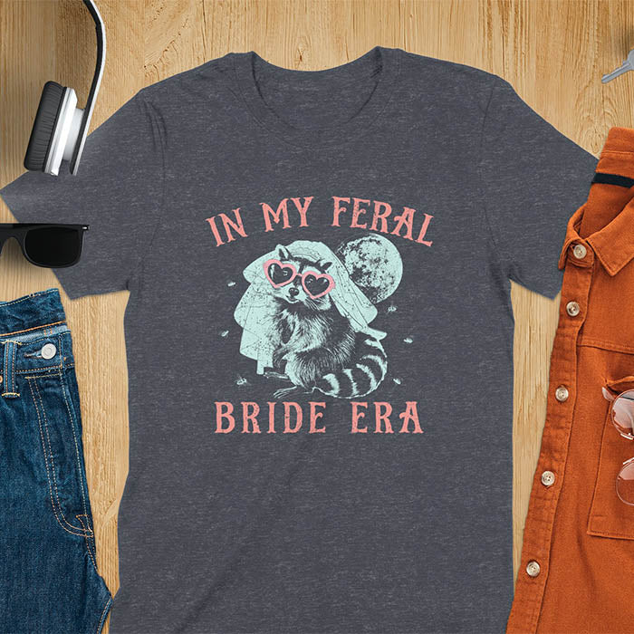 A raccoon wearing heart-shaped sunglasses and a bride's veil, with the moon in the background. Text reads In My Feral Bride Era.