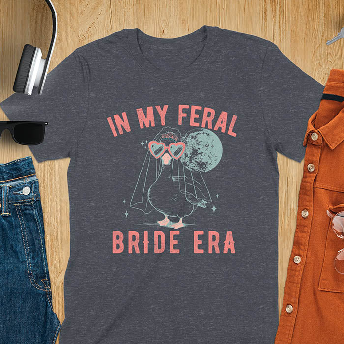 A goose standing, wearing heart-shaped sunglasses and a bride's veil. Moon in the upper right background. Retro-style text reads In My Feral on top Bride Era at bottom. Whimsical image.