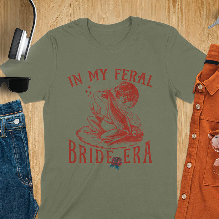 A vintage-style frog wearing a bride veil, croaking to the sky from a lily pad with a moon in the background. Text reads In My Feral Bride Era.