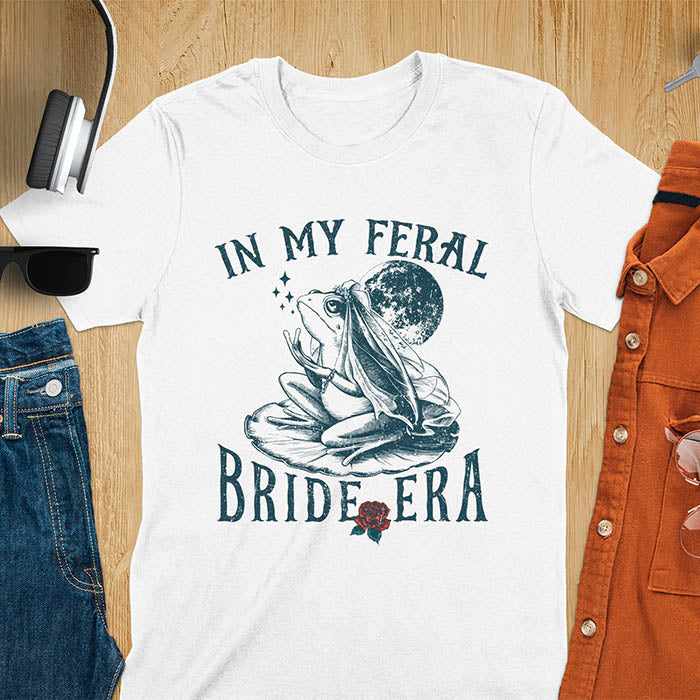 A vintage-style frog wearing a bride veil, croaking to the sky from a lily pad with a moon in the background. Text reads In My Feral Bride Era.