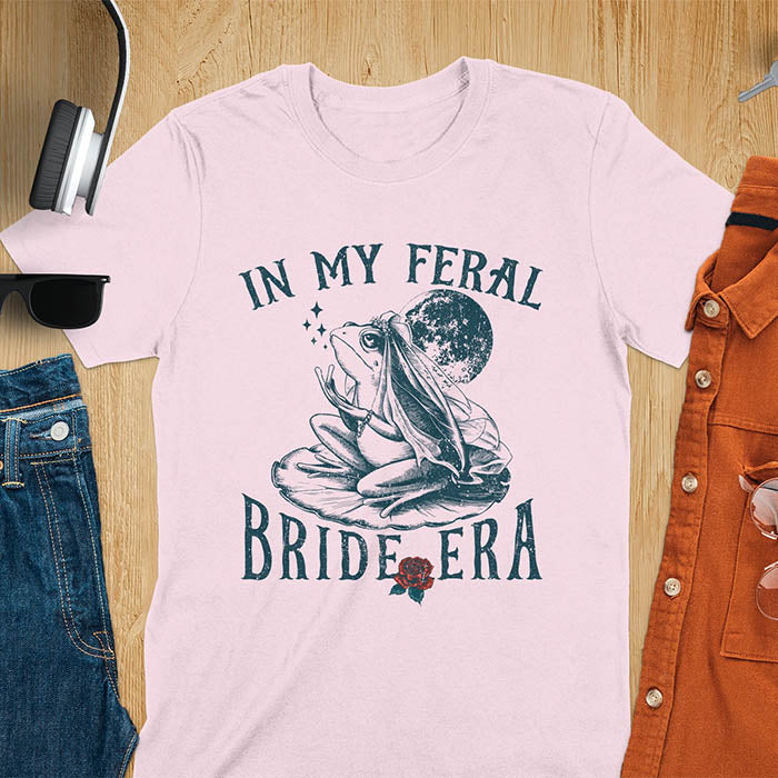A vintage-style frog wearing a bride veil, croaking to the sky from a lily pad with a moon in the background. Text reads In My Feral Bride Era.