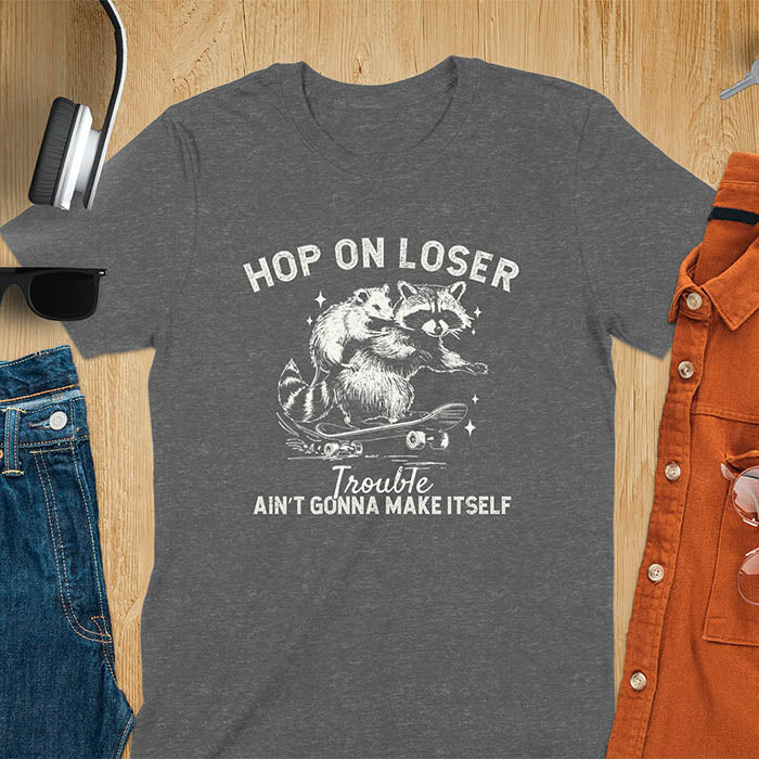 A raccoon riding a skateboard with an opossum on its back. Text reads Hop On Loser and Trouble Ain't Gonna Make Itself.