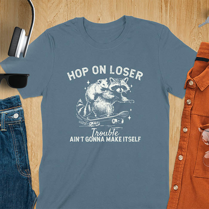 A raccoon riding a skateboard with an opossum on its back. Text reads Hop On Loser and Trouble Ain't Gonna Make Itself.
