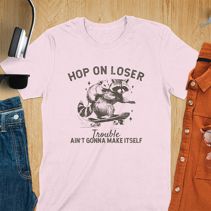 A raccoon riding a skateboard with an opossum on its back. Text reads Hop On Loser and Trouble Ain't Gonna Make Itself.