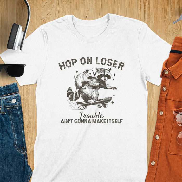 A raccoon riding a skateboard with an opossum on its back. Text reads Hop On Loser and Trouble Ain't Gonna Make Itself.