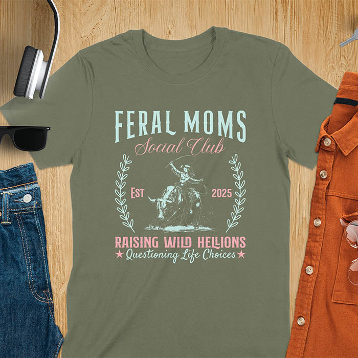 A t-shirt with a cowgirl riding a bucking bull. Text: Feral Moms SOCIAL CLUB above and Raising HELLIONS, questioning life choices below. This unhinged t-shirts design features a cowgirl mom on a rodeo bucking bull, a weird meme shirt for a feral mom gift. A retro inspired design, one of those shirts that go hard, a mama outfit or feral wife gift. A mom gift or gift for new mom for a western mama.