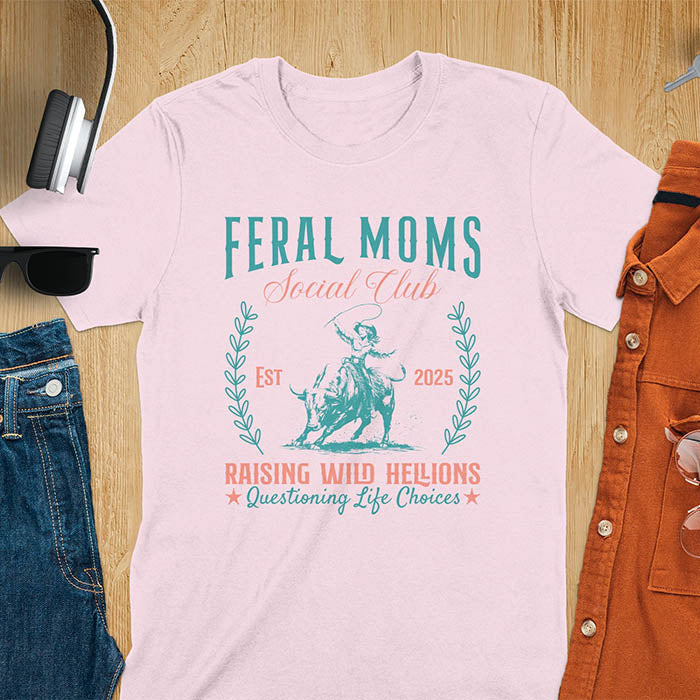 A t-shirt with a cowgirl riding a bucking bull. Text: Feral Moms SOCIAL CLUB above and Raising HELLIONS, questioning life choices below. This unhinged t-shirts design features a cowgirl mom on a rodeo bucking bull, a weird meme shirt for a feral mom gift. A retro inspired design, one of those shirts that go hard, a mama outfit or feral wife gift. A mom gift or gift for new mom for a western mama.