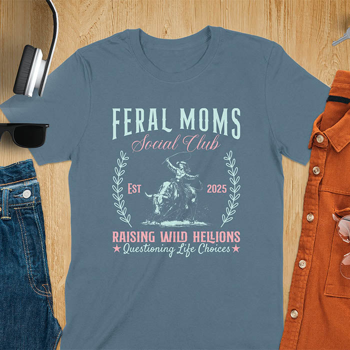 A t-shirt with a cowgirl riding a bucking bull. Text: Feral Moms SOCIAL CLUB above and Raising HELLIONS, questioning life choices below. This unhinged t-shirts design features a cowgirl mom on a rodeo bucking bull, a weird meme shirt for a feral mom gift. A retro inspired design, one of those shirts that go hard, a mama outfit or feral wife gift. A mom gift or gift for new mom for a western mama.