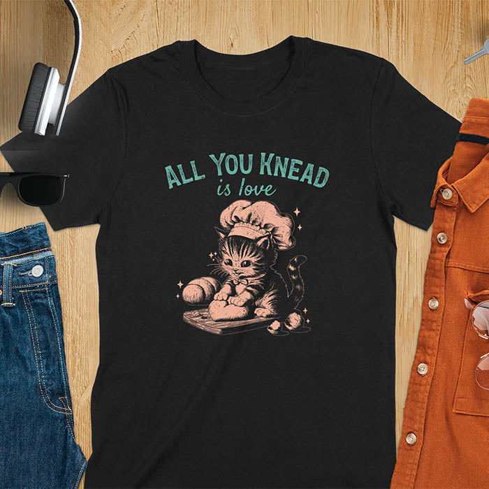 A t-shirt with a kitten wearing a chef's hat, kneading dough. Text: "ALL YOU knead" above and "is love" below. This Funny baking shirt is a Funny meme shirt showing kitten cuteness, a great cat lover gift and mom gift. An Animal lovers tshirt and cat person tee, a Pet cat owner gift. One of the Funny bakers gifts, a baker shirt gift, and a Funny cat t shirt.