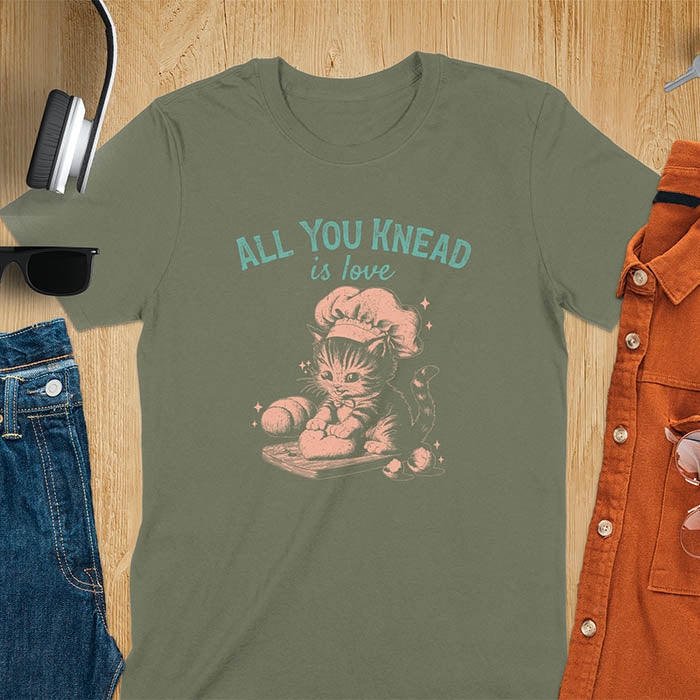A t-shirt with a kitten wearing a chef's hat, kneading dough. Text: "ALL YOU knead" above and "is love" below. This Funny baking shirt is a Funny meme shirt showing kitten cuteness, a great cat lover gift and mom gift. An Animal lovers tshirt and cat person tee, a Pet cat owner gift. One of the Funny bakers gifts, a baker shirt gift, and a Funny cat t shirt.