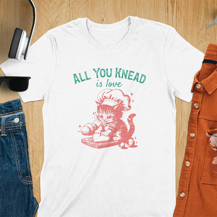 A t-shirt with a kitten wearing a chef's hat, kneading dough. Text: "ALL YOU knead" above and "is love" below. This Funny baking shirt is a Funny meme shirt showing kitten cuteness, a great cat lover gift and mom gift. An Animal lovers tshirt and cat person tee, a Pet cat owner gift. One of the Funny bakers gifts, a baker shirt gift, and a Funny cat t shirt.