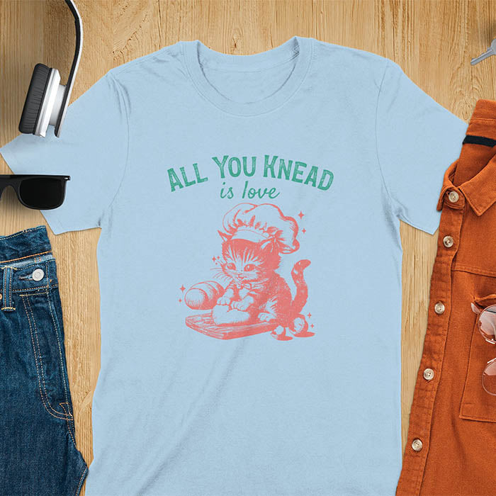 A t-shirt with a kitten wearing a chef's hat, kneading dough. Text: "ALL YOU knead" above and "is love" below. This Funny baking shirt is a Funny meme shirt showing kitten cuteness, a great cat lover gift and mom gift. An Animal lovers tshirt and cat person tee, a Pet cat owner gift. One of the Funny bakers gifts, a baker shirt gift, and a Funny cat t shirt.