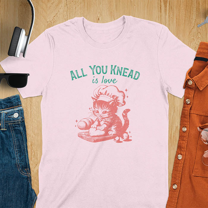 A t-shirt with a kitten wearing a chef's hat, kneading dough. Text: "ALL YOU knead" above and "is love" below. This Funny baking shirt is a Funny meme shirt showing kitten cuteness, a great cat lover gift and mom gift. An Animal lovers tshirt and cat person tee, a Pet cat owner gift. One of the Funny bakers gifts, a baker shirt gift, and a Funny cat t shirt.