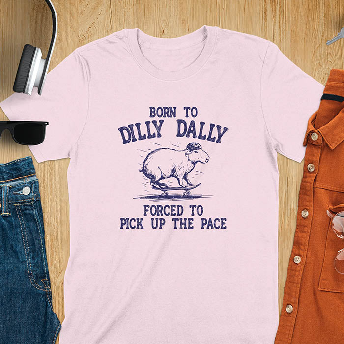 A capybara skateboarding, donning a protective helmet .Above it, the words "Born to dilly dally", while below, "Forced to pick up the pace". Rendered in a charming vintage font with a faded look.