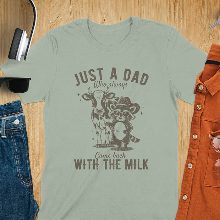 A t-shirt with a raccoon wearing a cowboy hat and sunglasses, holding a leash to a cow. Text: Just a Dad WHO ALWAYS above and Came Back WITH THE MILK below. This funny raccoon shirt features funny graphics, a dad t shirt for a funny fathers day or fathers day gift. A funny shirt for dad or gift for dad, a husband gift or father in law gifts. Could be used for a dad announcement, expectant dad, or godfather proposal.