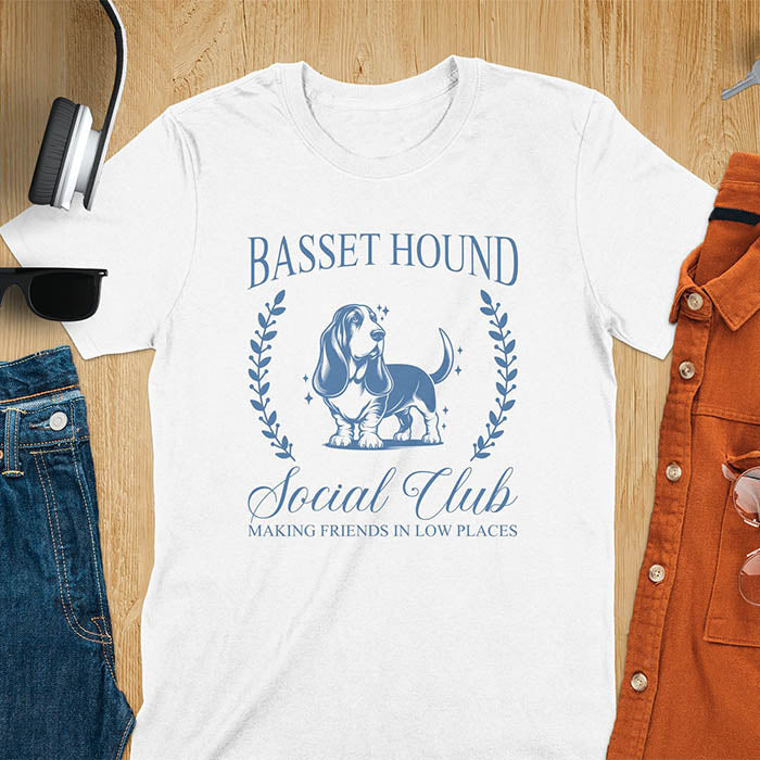 A t-shirt featuring a vintage-style basset hound design in muted blue. Includes Basset Hound, Social Club, Short & Sweet Forever text, laurel wreaths, EST 2024, and a centered dog illustration for a timeless, elegant look.