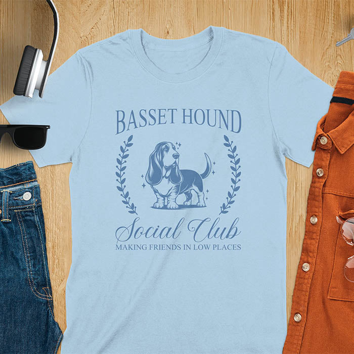A t-shirt featuring a vintage-style basset hound design in muted blue. Includes Basset Hound, Social Club, Short & Sweet Forever text, laurel wreaths, EST 2024, and a centered dog illustration for a timeless, elegant look.