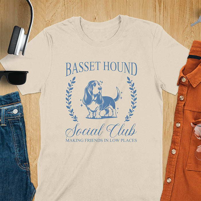 A t-shirt featuring a vintage-style basset hound design in muted blue. Includes Basset Hound, Social Club, Short & Sweet Forever text, laurel wreaths, EST 2024, and a centered dog illustration for a timeless, elegant look.