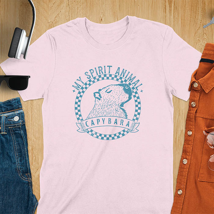 A T-shirt with a graphic of a capybara inside a checkered circle. Above the capybara, text reads "MY SPIRIT ANIMAL," and below, a banner says "CAPYBARA."