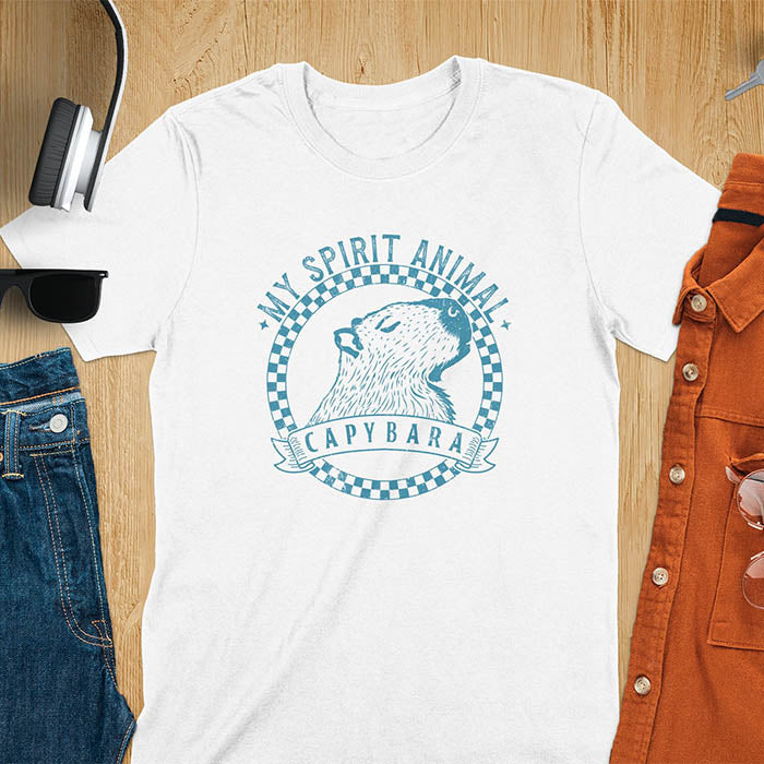 A T-shirt with a graphic of a capybara inside a checkered circle. Above the capybara, text reads "MY SPIRIT ANIMAL," and below, a banner says "CAPYBARA."