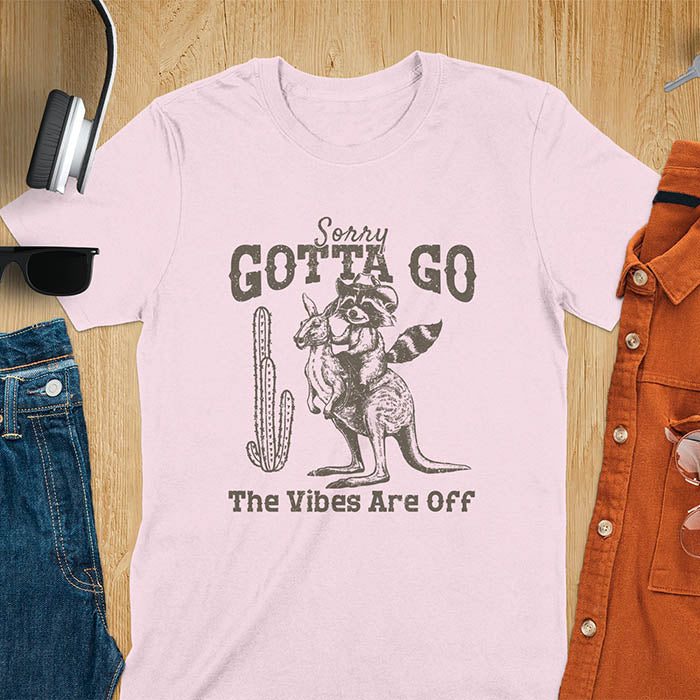 A t-shirt with a raccoon wearing a cowboy hat riding a kangaroo. Text: Sorry GOTTA GO above and The Vibes Are Off below. This humorous tee-shirt features a funny gen z meme and sarcastic meme shirt, a weird graphics shirt.  A funny retro graphic and vintage graphic tee with rodeo cowboy elements. A silly shirt or funny unhinged shirt, an animal person gift or kangaroo gifts. A raccoon t shirt or mom gift alternative.