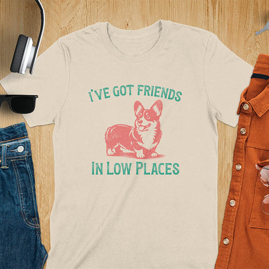 Our vintage-inspired design features a cute corgi silhouette with facial details. Text above it says 'I've Got Friends' and below it says ''In Low Places.' With its retro vibe and distressed texture, this tee adds a touch of nostalgia to your wardrobe.