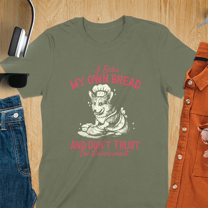 A t-shirt with a corgi wearing a chef's hat and apron, kneading dough. Text: "I Bake MY OWN BREAD" above and "AND DON'T TRUST The Government" below. This retro sarcastic tee is a funny meme shirt and funny dog shirt, a corgi shirt for a corgi lovers gift. An animal lovers tshirt and dog lover gift, a dog mom shirt or pet dad shirt. A dog person tee and pet dog owner gift, one of the funny bakers gifts, a gift for mom or her.