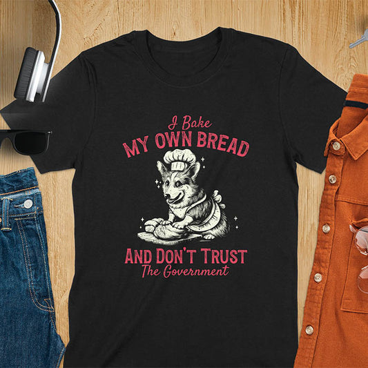 A t-shirt with a corgi wearing a chef's hat and apron, kneading dough. Text: "I Bake MY OWN BREAD" above and "AND DON'T TRUST The Government" below. This retro sarcastic tee is a funny meme shirt and funny dog shirt, a corgi shirt for a corgi lovers gift. An animal lovers tshirt and dog lover gift, a dog mom shirt or pet dad shirt. A dog person tee and pet dog owner gift, one of the funny bakers gifts, a gift for mom or her.