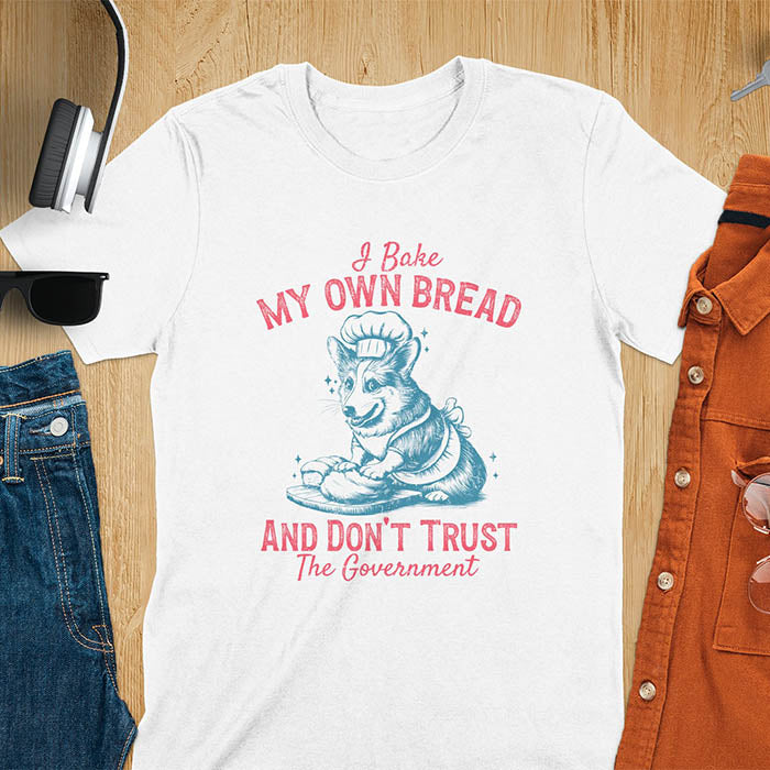 A t-shirt with a corgi wearing a chef's hat and apron, kneading dough. Text: "I Bake MY OWN BREAD" above and "AND DON'T TRUST The Government" below. This retro sarcastic tee is a funny meme shirt and funny dog shirt, a corgi shirt for a corgi lovers gift. An animal lovers tshirt and dog lover gift, a dog mom shirt or pet dad shirt. A dog person tee and pet dog owner gift, one of the funny bakers gifts, a gift for mom or her.