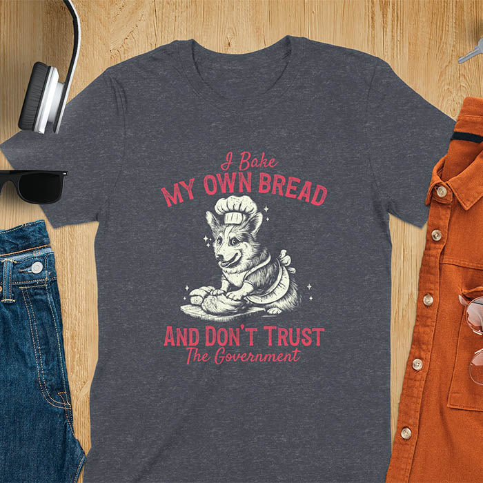 A t-shirt with a corgi wearing a chef's hat and apron, kneading dough. Text: "I Bake MY OWN BREAD" above and "AND DON'T TRUST The Government" below. This retro sarcastic tee is a funny meme shirt and funny dog shirt, a corgi shirt for a corgi lovers gift. An animal lovers tshirt and dog lover gift, a dog mom shirt or pet dad shirt. A dog person tee and pet dog owner gift, one of the funny bakers gifts, a gift for mom or her.