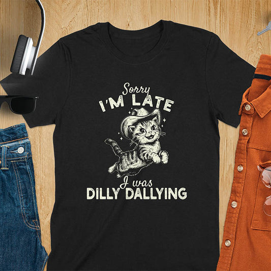 A t-shirt with a tabby cat wearing a cowboy hat. Text: Sorry I'M LATE above and I was DILLY DALLYING below. This cat lover shirt features cat cuteness gift and kawaiiness cuteness. A sarcastic meme shirt about dilly dallying, a funny genz meme with funny animals. This cowboy cat design has retro aesthetics, a snarky humorous tee, an animal person gift or mom gift.