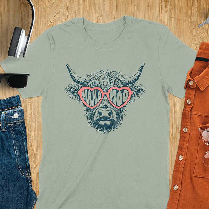A t-shirt featuring a fluffy highland cow face with long horns, wearing pink heart-shaped sunglasses spelling MAMA MOO. Below the cow, Veronica is written in script font. This retro mom tee-shirt design is a cute cow highlander for mama mom life. A funny animal mom tee for an expecting mom or pregnant mom gift, ideal for a pregnancy announcement or pregnancy reveal. A great mom gift or Mother days gift, or a new mom gift for a gift for wife. The name can be personalized.