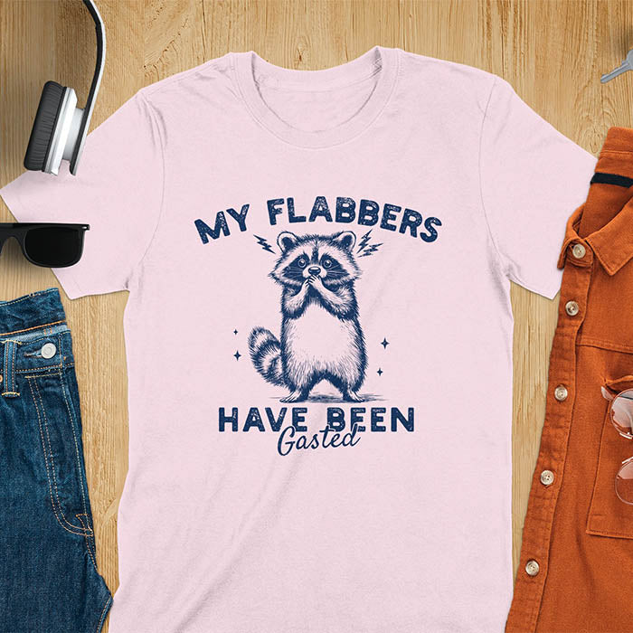 A t-shirt featuring a raccoon with wide eyes and paws covering its mouth. Text: MY FLABBERS above and HAVE BEEN Gasted below in a distressed font. This sarcastic tee-shirt features a funny raccoon with kawaiiness cuteness, a genz meme tee or anxiety tshirt. A depress meme and weirdcore memes design, a funny gag gift for sad core fans. This is one of those shirts that go hard, a trash panda design.