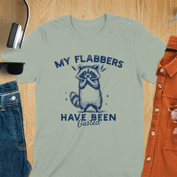 A t-shirt featuring a raccoon with wide eyes and paws covering its mouth. Text: MY FLABBERS above and HAVE BEEN Gasted below in a distressed font. This sarcastic tee-shirt features a funny raccoon with kawaiiness cuteness, a genz meme tee or anxiety tshirt. A depress meme and weirdcore memes design, a funny gag gift for sad core fans. This is one of those shirts that go hard, a trash panda design.