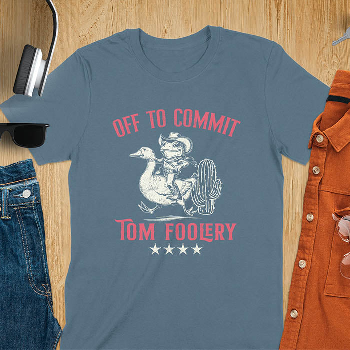 A t-shirt with a frog dressed as a rodeo cowboy riding a goose. Text: "Off To COMMIT" above and "TOM FOOLERY" below. This meme t shirt features a funny frog tee and silly funny goose, a weird graphics shirt. A funny genz meme and unhinged tee-shirt, with rodeo cowboy and cowgirl t shirt elements. A retro aesthetic and western style gift, an animal person gift. A mom gift alternative.