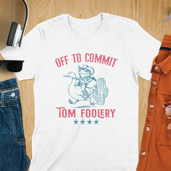 A t-shirt with a frog dressed as a rodeo cowboy riding a goose. Text: "Off To COMMIT" above and "TOM FOOLERY" below. This meme t shirt features a funny frog tee and silly funny goose, a weird graphics shirt. A funny genz meme and unhinged tee-shirt, with rodeo cowboy and cowgirl t shirt elements. A retro aesthetic and western style gift, an animal person gift. A mom gift alternative.