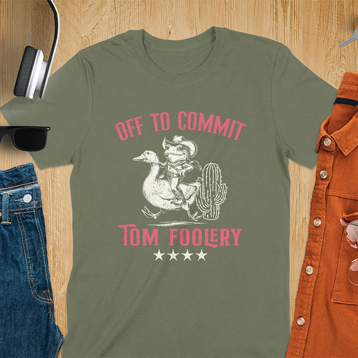 A t-shirt with a frog dressed as a rodeo cowboy riding a goose. Text: "Off To COMMIT" above and "TOM FOOLERY" below. This meme t shirt features a funny frog tee and silly funny goose, a weird graphics shirt. A funny genz meme and unhinged tee-shirt, with rodeo cowboy and cowgirl t shirt elements. A retro aesthetic and western style gift, an animal person gift. A mom gift alternative.