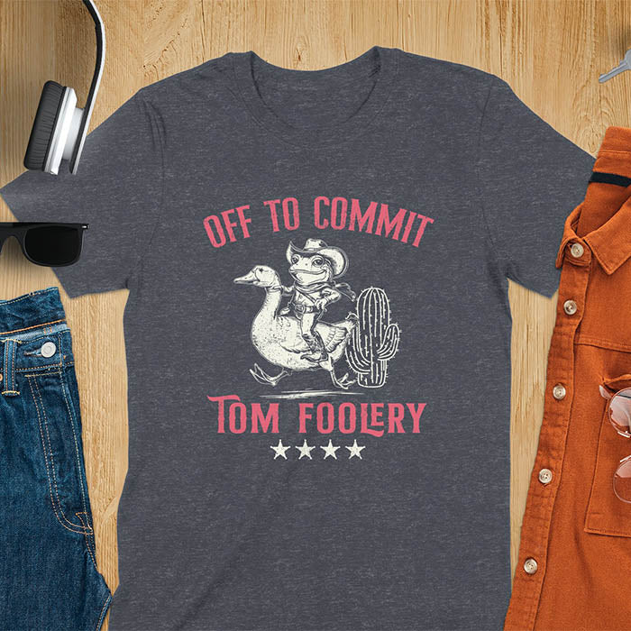 A t-shirt with a frog dressed as a rodeo cowboy riding a goose. Text: "Off To COMMIT" above and "TOM FOOLERY" below. This meme t shirt features a funny frog tee and silly funny goose, a weird graphics shirt. A funny genz meme and unhinged tee-shirt, with rodeo cowboy and cowgirl t shirt elements. A retro aesthetic and western style gift, an animal person gift. A mom gift alternative.