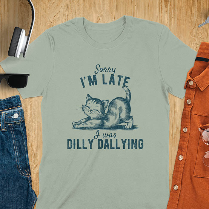 A t-shirt with a kitten stretching its back. Text: Sorry I'M LATE above and I was DILLY DALLYING below. This cat lover shirt features cat cuteness gift and kawaiiness cuteness. A sarcastic meme shirt about dilly dally, a funny genz meme with funny animals. This kawaii kitten design has vintage aesthetics, a snarky humorous tee, an animal person gift or mom gift hers. A cat mom t shirt alternative.